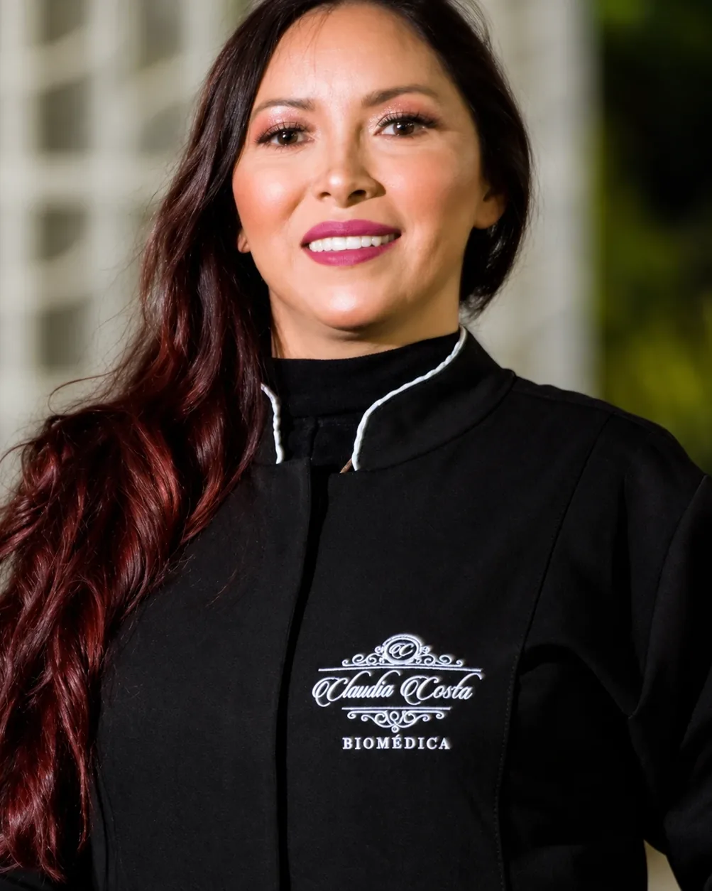 Dra. Claudineia Costa, biomédica esteta, sorrindo, de jaleco preto com o nome bordado